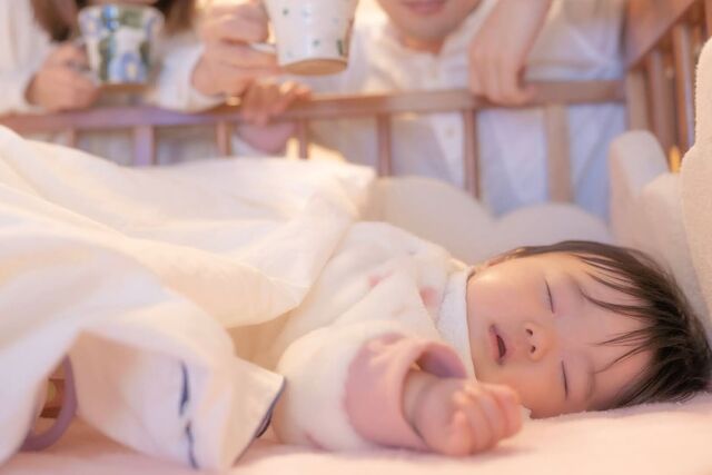 赤ちゃんが眠る姿を見つめる両親